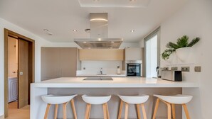Una cocina moderna con una isla central, taburetes de bar, horno empotrado y una planta en la pared.