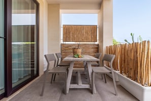 Een moderne eethoek buiten, met een houten tafel en stoelen, een gevlochten mand en een bamboebeschoeiing.