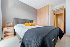 Ein Schlafzimmer mit Bett, Nachttisch, Lampe, Kleiderschrank und einer Tür.