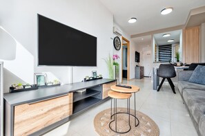 Een moderne woonkamer met een flatscreen televisie, een bank, een salontafel en een eethoek op de achtergrond.