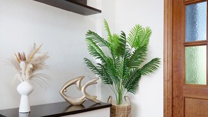Une pièce avec un comptoir en bois foncé, un vase blanc contenant des plantes séchées, un objet décoratif doré et une plante verte dans un pot en osier.