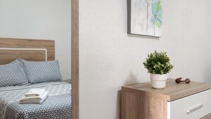 Un lit bien fait, avec une literie à motifs, une table de chevet ornée d’une plante en pot et une œuvre d’art accrochée au mur.