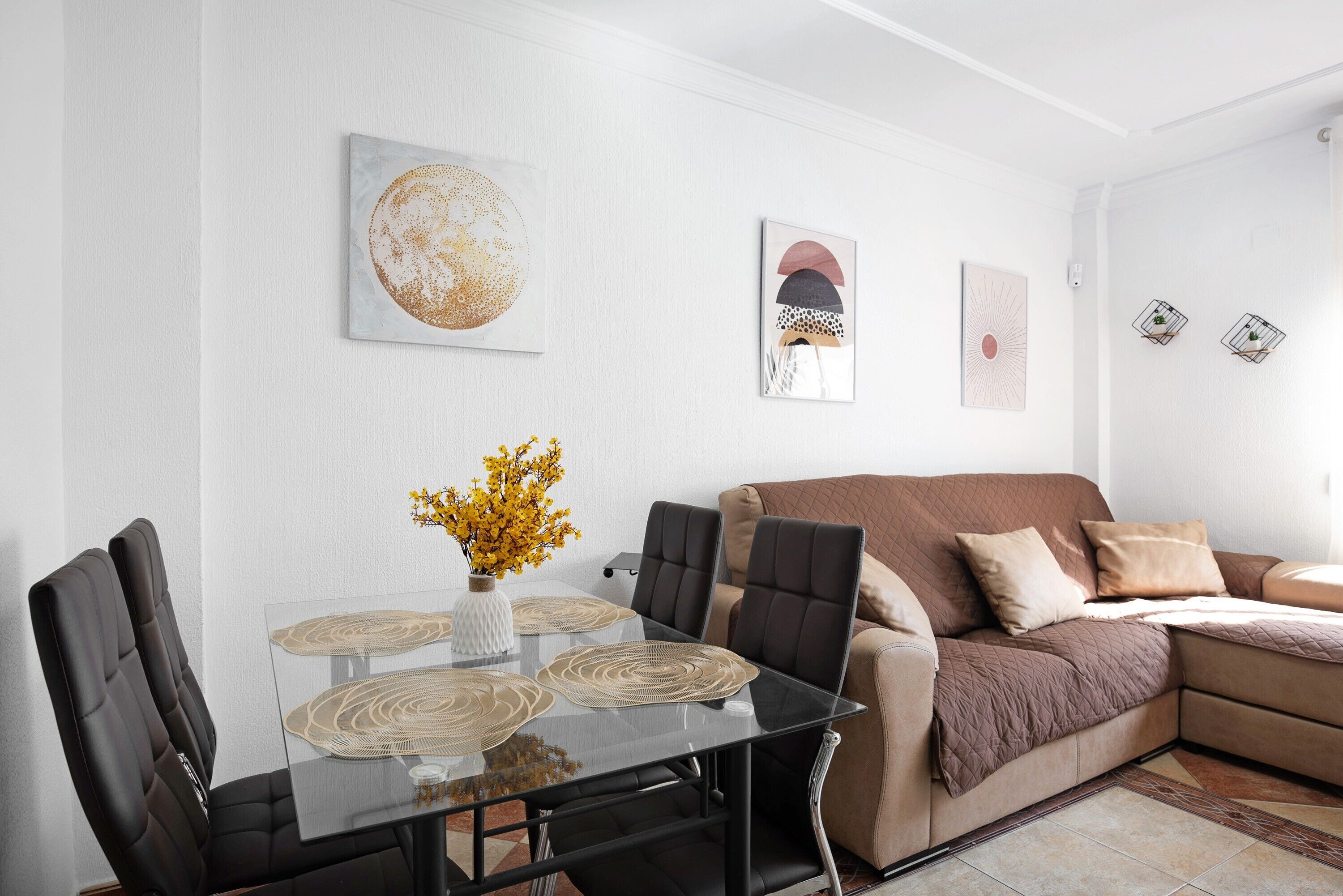 Ein modernes Wohnzimmer mit einem Glastisch, schwarzen Stühlen, einem braunen Sofa und Wanddekoration.