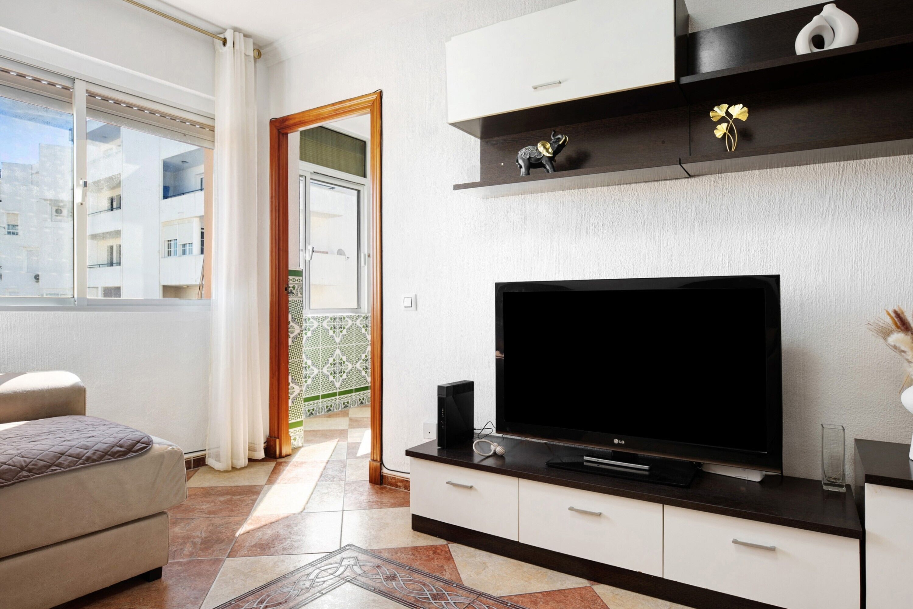 A modern living room with a flat-screen TV, a sofa, a coffee table, and a decorative shelf.