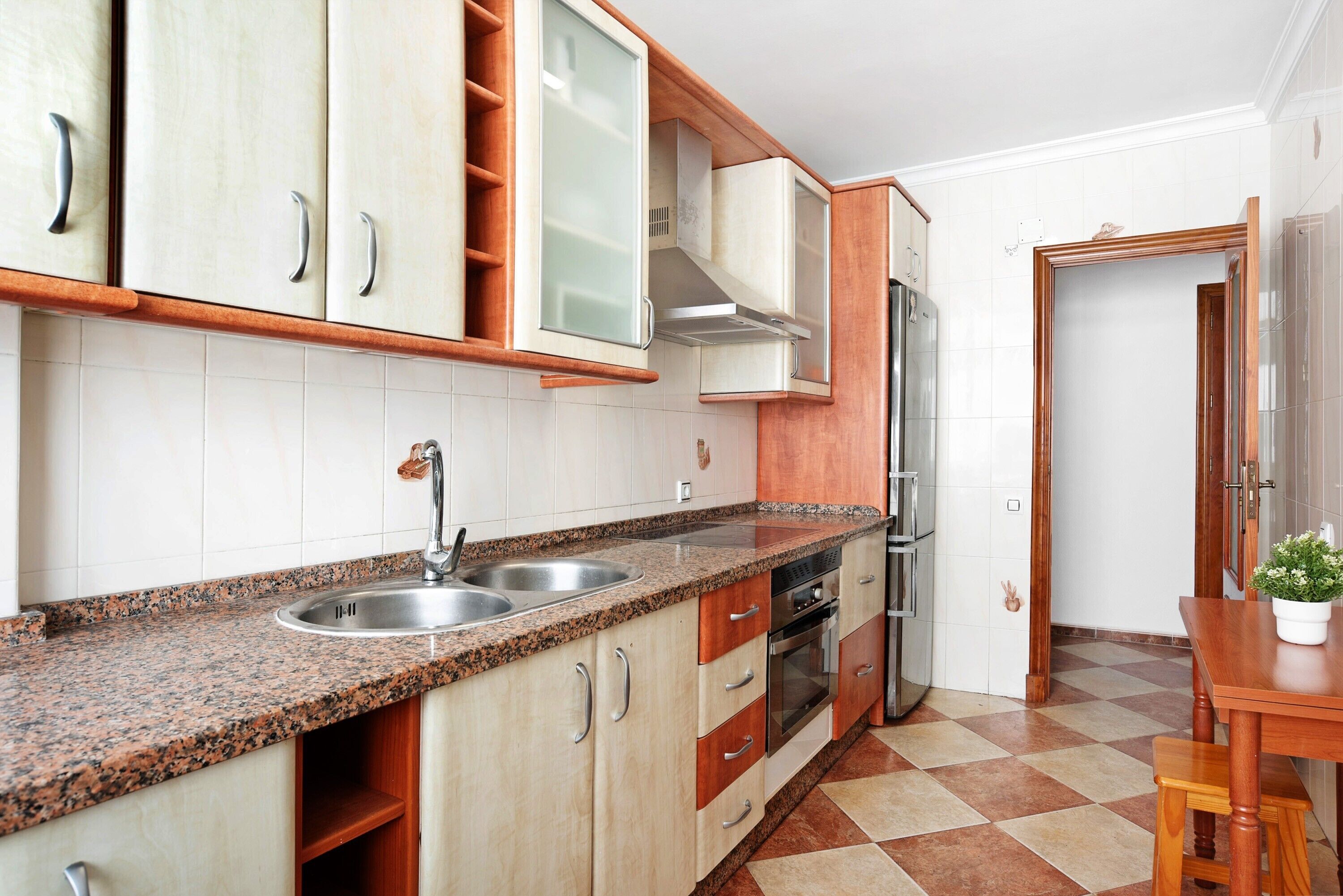 A kitchen with granite countertops, stainless steel appliances, wooden cabinets, and a tiled floor.