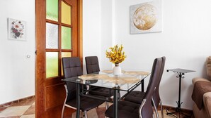 Un coin repas avec une table en verre, des chaises noires, un vase rempli de fleurs jaunes et un tableau accroché au mur.