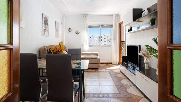 Un salon moderne comprenant un coin repas, un canapé, un téléviseur et une fenêtre donnant sur la ville.