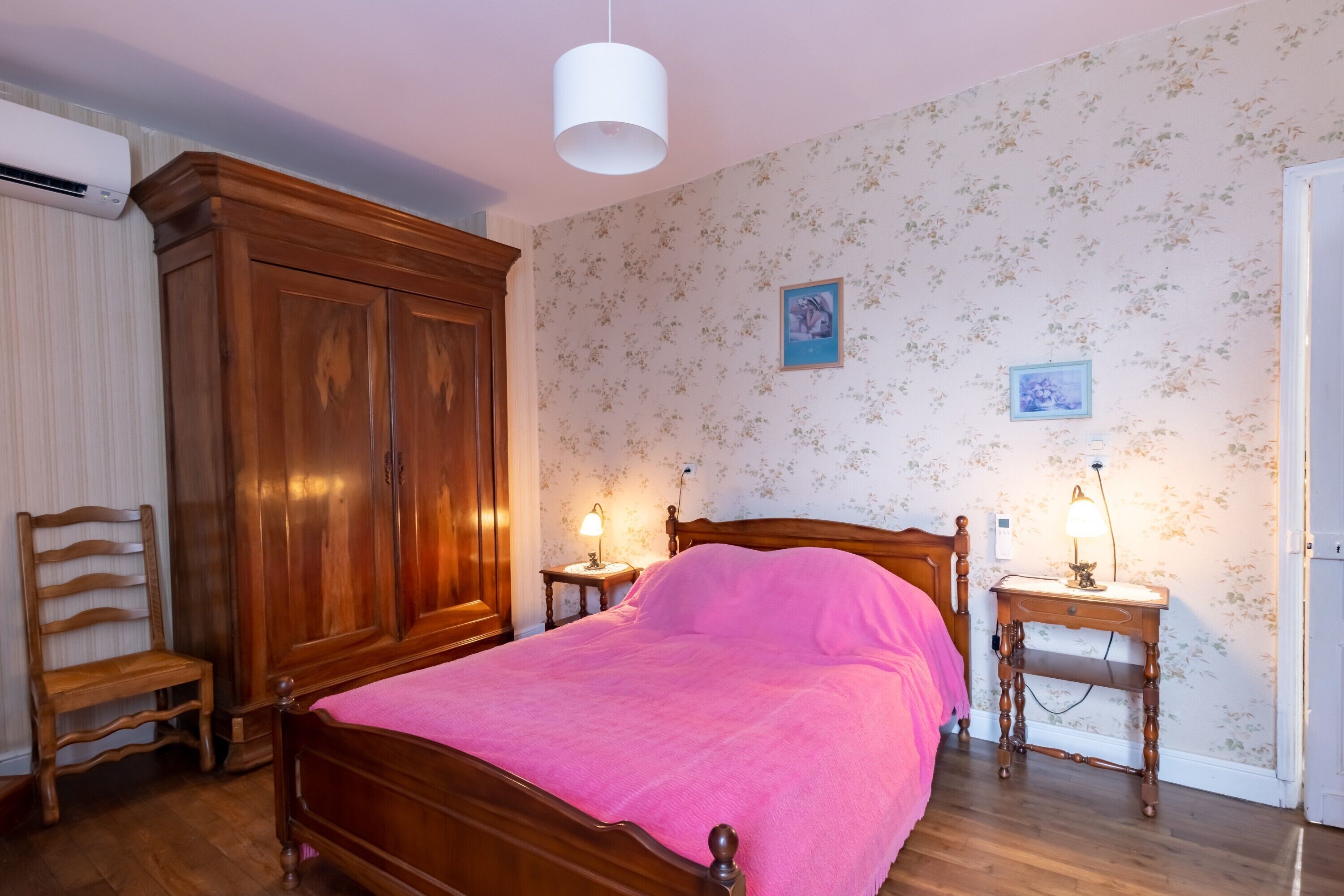 Een slaapkamer met een houten bed, twee nachtkastjes met lampen, een houten garderobe en bloemenbehang.