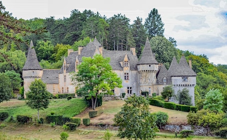 A castle with multiple towers, surrounded by lush greenery and a hilly landscape.. Holiday Home 'Le Haut Picot' with Private Terrace, Wi-Fi and Air Conditioning