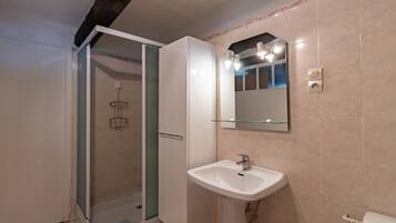 Un bagno con cabina doccia in vetro, lavandino bianco, specchio e WC.
