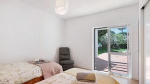 Ein Schlafzimmer mit zwei Betten, einem Sessel und einer Schiebetür zu einem Außenbereich.