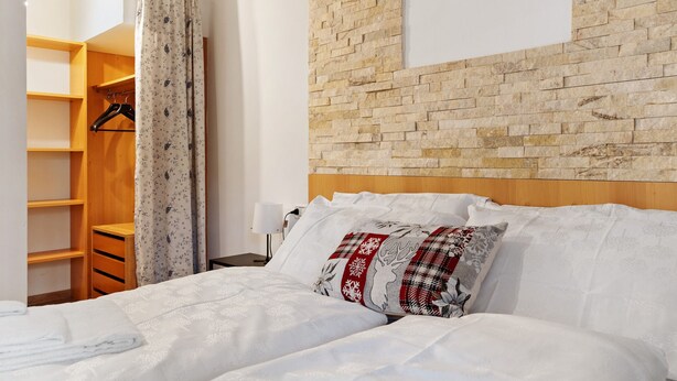 Ein Schlafzimmer mit einem hölzernen Kopfende, einem Bett mit weißer Bettwäsche, einem gemusterten Kissen, einem Holzschrank und einem Vorhang.