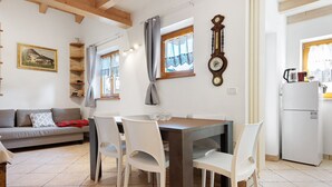 Ein Essbereich mit Tisch und Stühlen, einer Couch, einer Uhr und einem Kühlschrank.