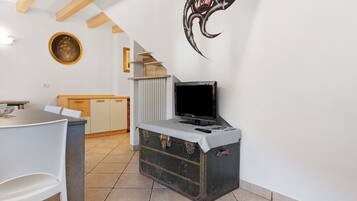 Una stanza con un tavolo da pranzo, una televisione su una valigia vintage, un termosifone e una scala.