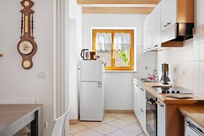 A compact kitchen with a refrigerator, stove, and a window with curtains.