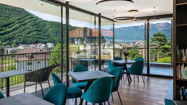 A modern dining area with tables and chairs, large windows with a mountain view, and a wooden floor. - Apartment "Erbacher - Renate's Gründer Suite" with Mountain View, Shared Pool & Sauna (Bozen)