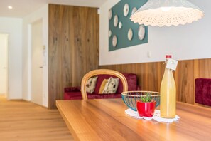 A wooden dining table with a bottle and a red bowl with plants.