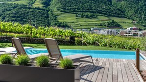 A poolside area with lounge chairs and a view of a vineyard and hills. - Apartment "Erbacher - Renate's Gründer Suite" with Mountain View, Shared Pool & Sauna (Bozen)