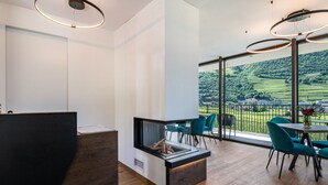 A modern interior with a reception desk, a fireplace, and a dining area with chairs and a table. - Apartment "Erbacher - Renate's Gründer Suite" with Mountain View, Shared Pool & Sauna (Bozen)