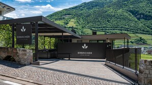A building with a sign reading 'ERBACHER LIVING NATURE' and a view of green hills in the background. - Apartment "Erbacher - Anna's Garten Suite" with Mountain View, Shared Pool & steam bath (Bozen)