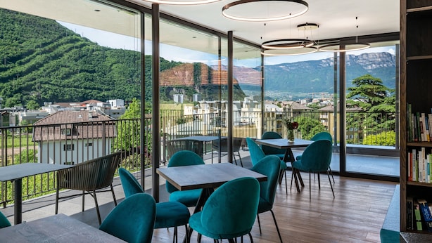 A modern dining area with tables and chairs, large windows with a mountain view, and a wooden floor. - Apartment "Erbacher - Anna's Garten Suite" with Mountain View, Shared Pool & steam bath (Bozen)