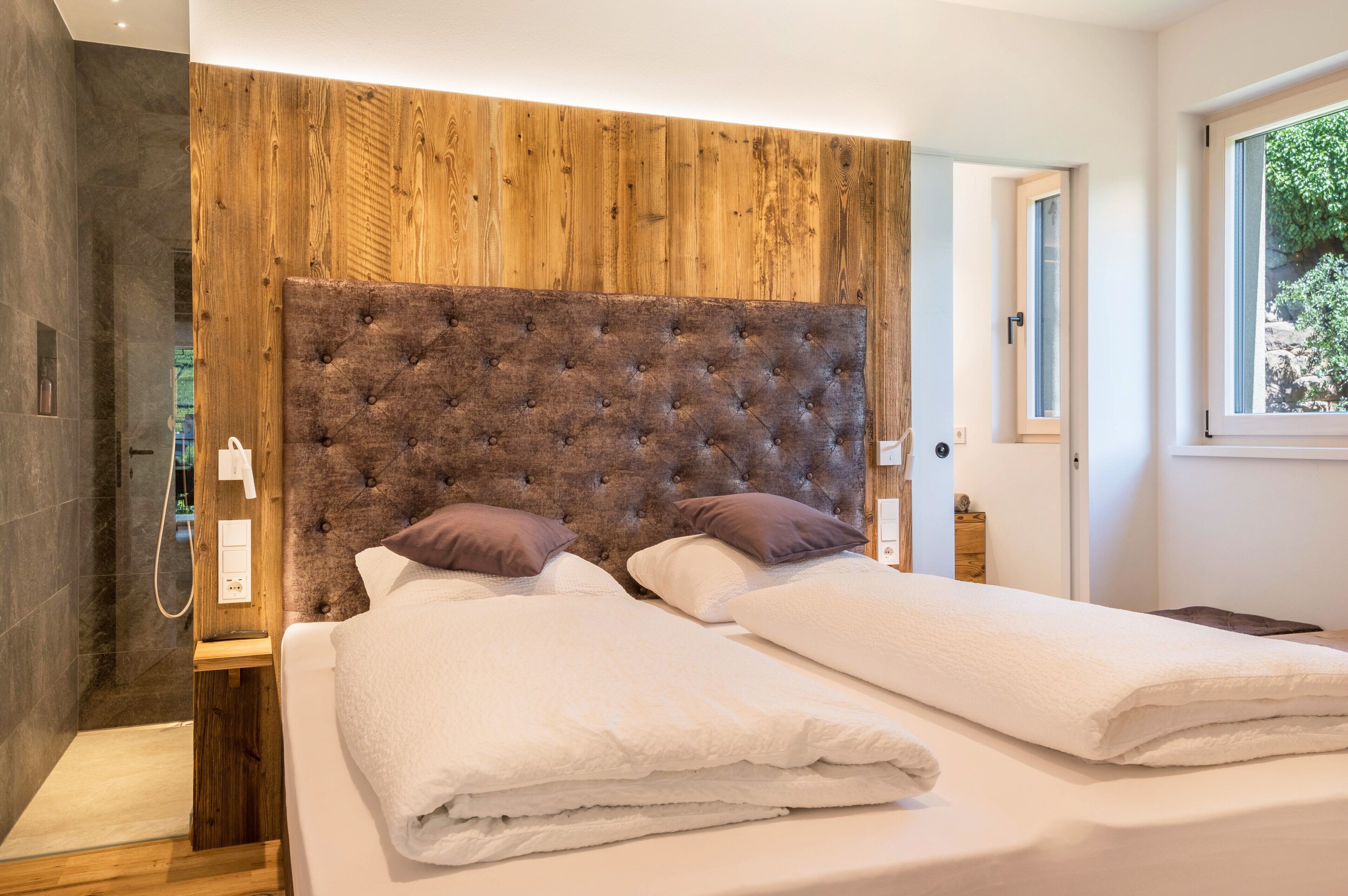 Une chambre à coucher avec une tête de lit en bois, deux lits, une table de chevet et une fenêtre.