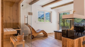 A modern interior with a wooden bench, a glass partition, a wooden rocking chair, a fireplace, and a view of mountains through a window.