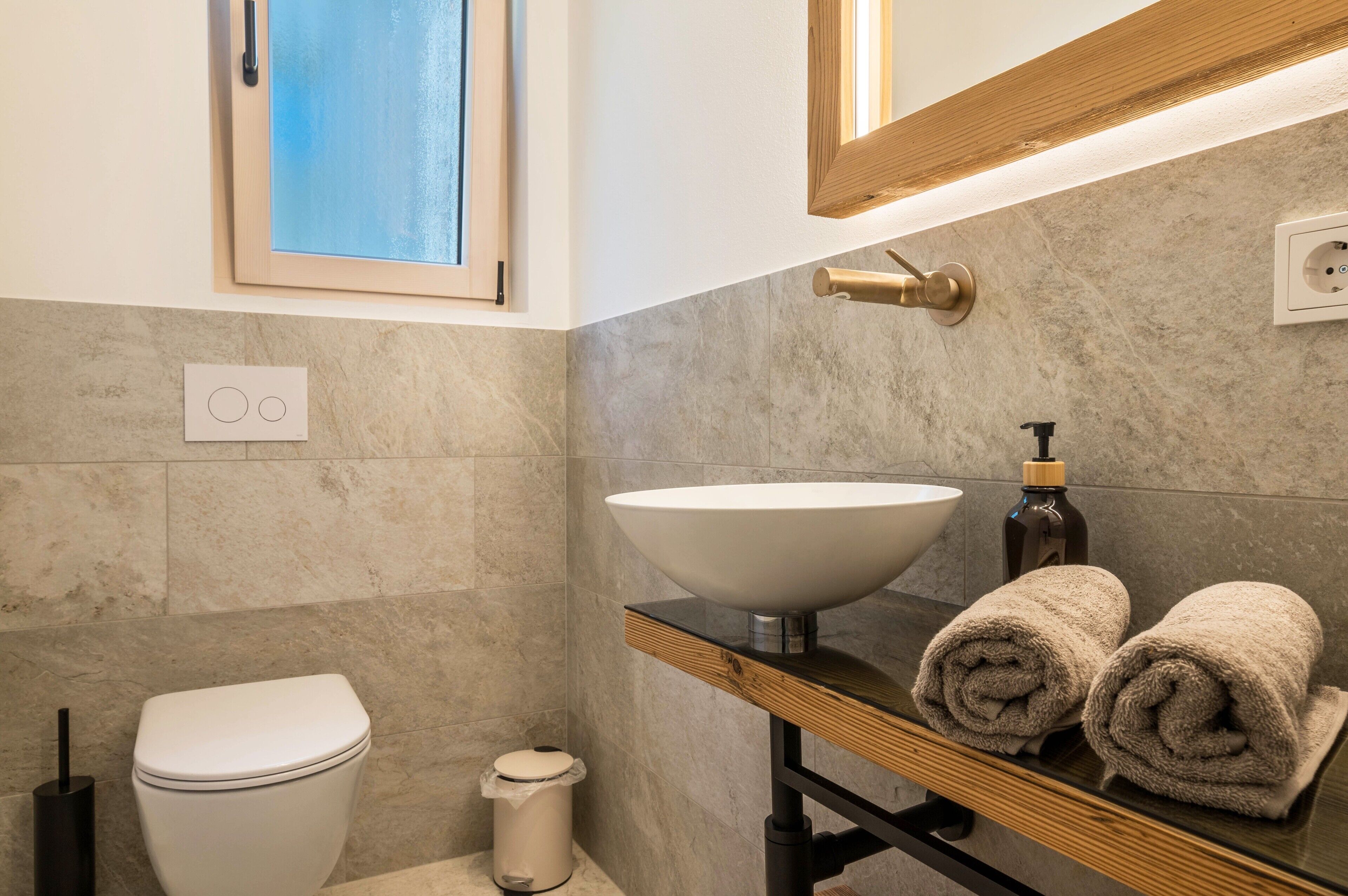 Une salle de bain équipée de toilettes, d’un lavabo, d’un miroir, d’une fenêtre et de serviettes posées sur le comptoir.