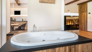 A modern bathroom with a freestanding bathtub, wooden accents, and a visible kitchen area in the background.