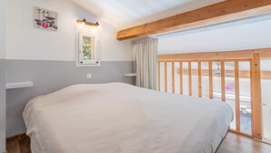 Een slaapkamer met een groot bed, houten balken, een raam met gordijnen en een balkon met een hekwerk.