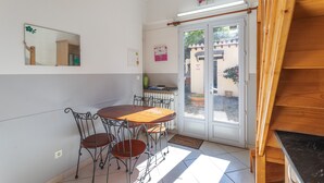 Een eetruimte met een ronde tafel en vier stoelen, een spiegel aan de muur, een deur naar buiten en een kleine plant op de vensterbank.
