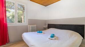 Een slaapkamer met een bed, een radiator, een raam met gordijnen en een houten plafond.
