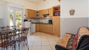 Een compacte keuken met houten kastjes, een eettafel met stoelen, een magnetron en een plafondventilator.