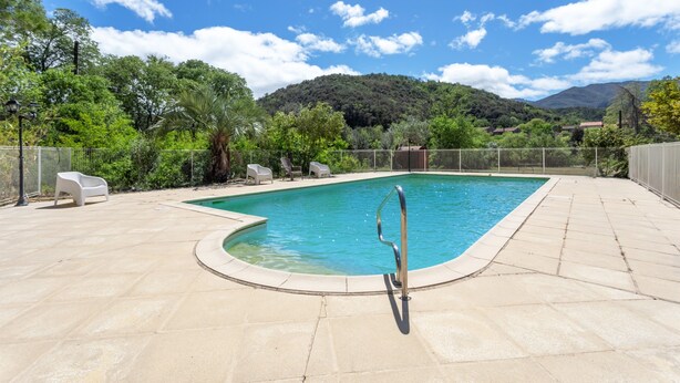 Une piscine avec un escalier en métal, entourée d’une terrasse carrelée et de chaises, avec une chaîne de montagnes en arrière-plan.