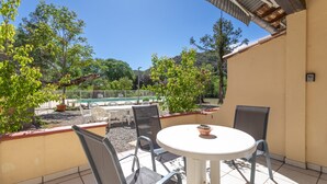 Une terrasse avec une table ronde et des chaises, une piscine en arrière-plan et une vue sur des arbres et des collines.
