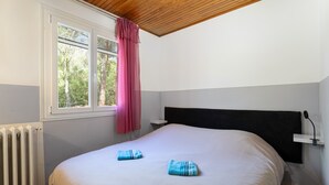 Une chambre avec un lit, une fenêtre donnant sur un beau paysage, un radiateur et un plafond en bois.