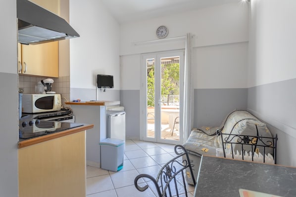 A compact kitchen with a microwave, toaster, and stove, a small refrigerator, a television, and a sliding glass door leading to an outdoor area.