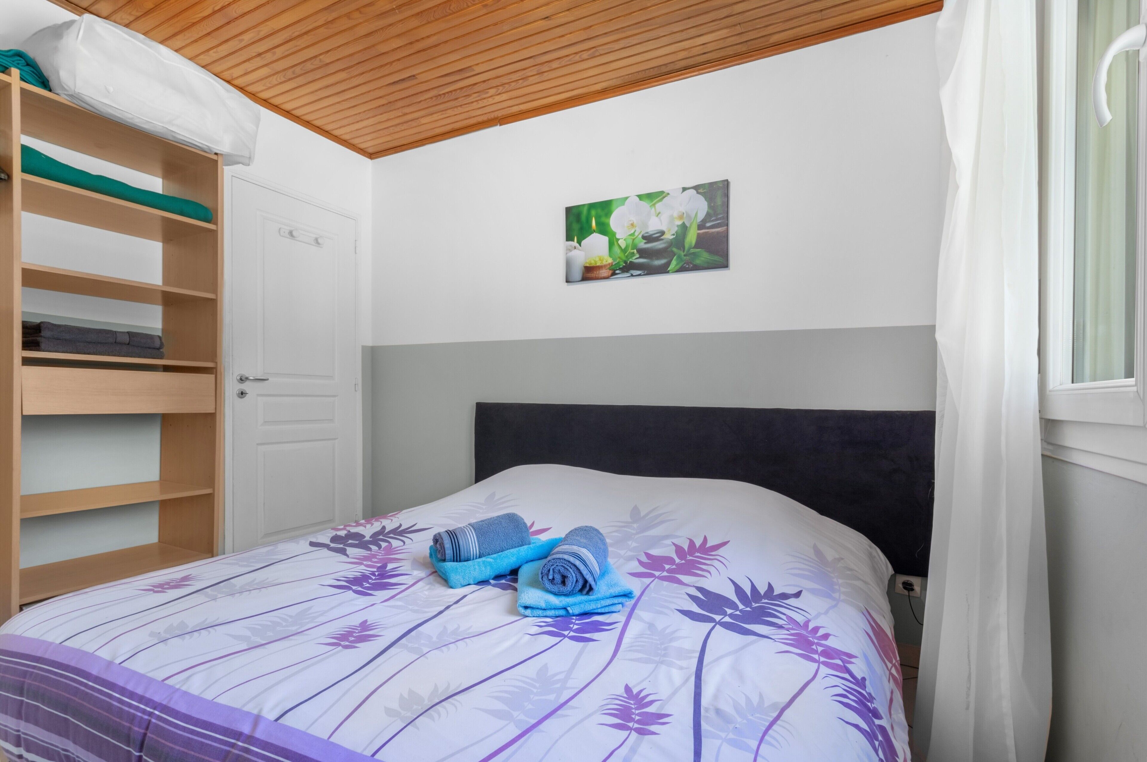 A bedroom with a bed, a wooden shelf unit, a white door, and a wall-mounted picture.