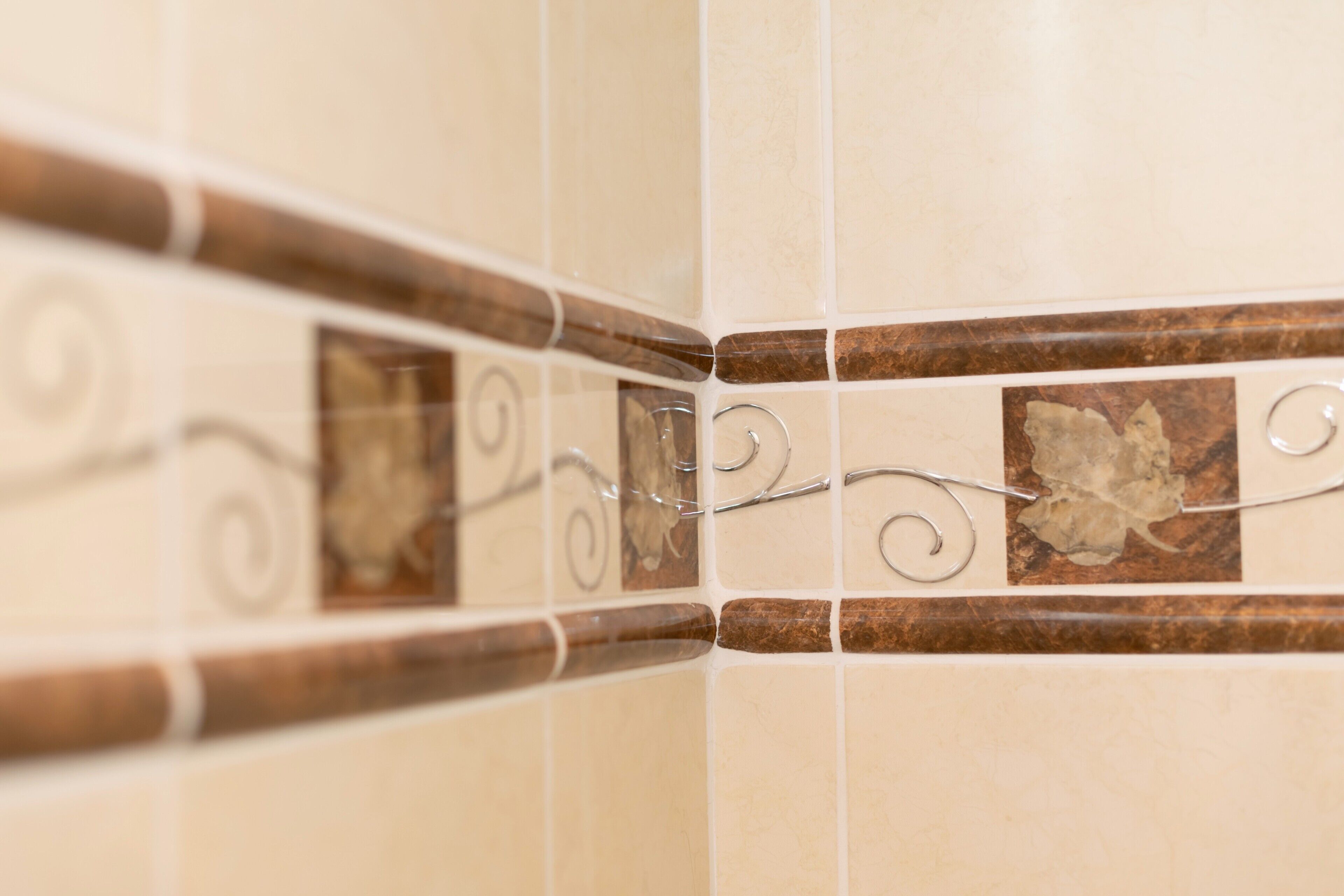 Een hoek van een betegelde muur met decoratieve metalen details en een bruine accenttegel.