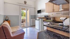 A compact kitchen with a microwave, toaster, and coffee machine, a small refrigerator, and a television above the counter.