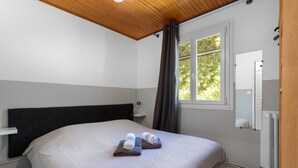 A bedroom with a bed, a nightstand, a window with curtains, and a mirror on the wall.