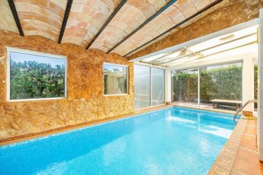 An indoor swimming pool with stone walls, large windows, and a view of greenery.