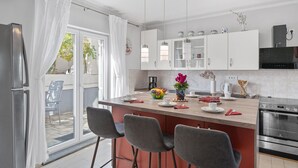 Et moderne køkken med hvide skabe, en central ø med barstole, en indbygget ovn og udsigt gennem glasdøren.