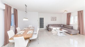 Een moderne woonkamer met een eethoek, een grijze hoekbank en een houten eettafel met witte stoelen.