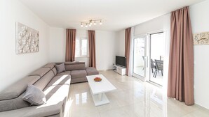Een moderne woonkamer met een modulaire bank, een flatscreen televisie, een salontafel en een schuifpui die leidt naar een buitenruimte.