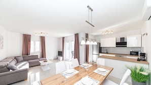Een moderne woonkamer met een bank, een eettafel voor vier personen en een keuken met apparatuur.