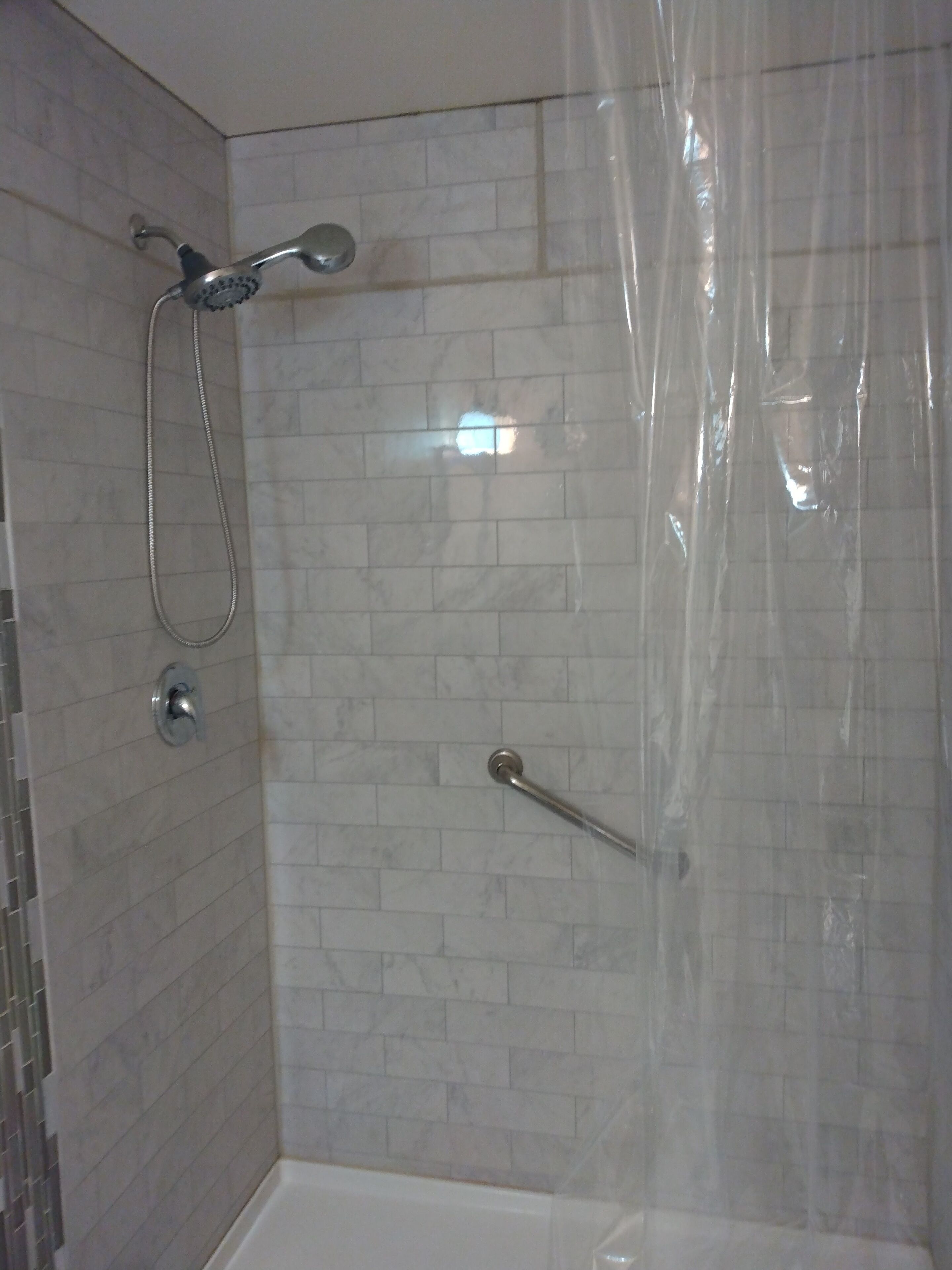 Ducha con cabezal de ducha manual y un accesorio de ducha manual, puerta de cristal y pared con azulejos.