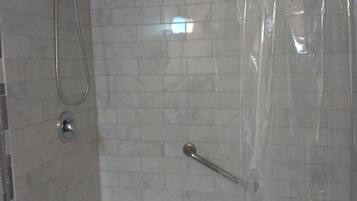 Ducha con cabezal de ducha manual y un accesorio de ducha manual, puerta de cristal y pared con azulejos.