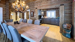Een rustiek houten blokhut interieur met een eethoek, bestaande uit een houten tafel en grijze fauteuils.