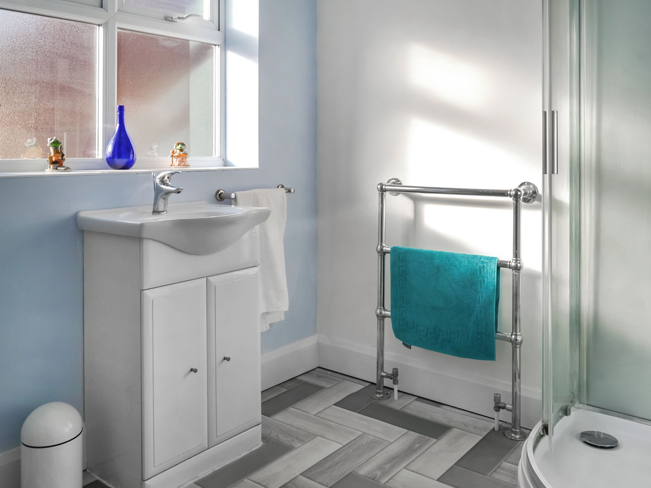 A bathroom with a white sink, a glass shower enclosure, and a blue towel on the towel rack.